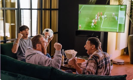 Three men engrossed in a soccer game, sitting on a couch, cheering and enjoying the match together